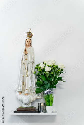 Statues of Holy Women in the Roman Catholic Church A statue of Mary stands on a stand next to a vase with flowers of roses