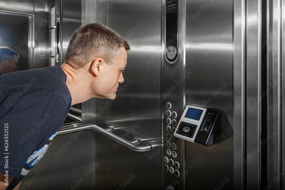 A man shows his face to a fingerprint access control terminal with a facial recognition function installed in the elevator
