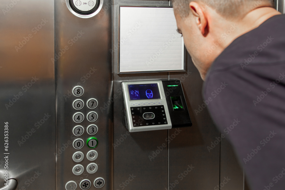 A man shows his face to a fingerprint access control terminal with a facial recognition function installed in the elevator