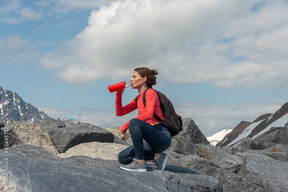 Woman hiker drinks water from a glass bottle while taking break while hiking up a mountain.