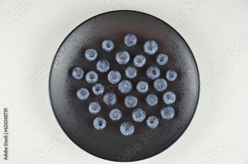 A bunch of blueberries on a black textured plate on a white background, top view