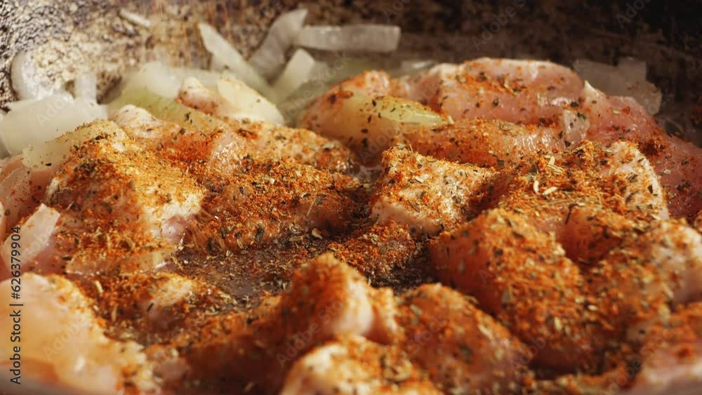 Pieces of chicken fried in a cast-iron skillet in oil with onions sprinkled with spices Pieces of chicken fried in a cast-iron skillet in oil with onions sprinkled with spices