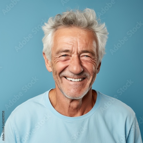 Portrait of a smiling elderly man with gray hair. Closeup face of a handsome Caucasian old man looking at the camera on a blue background. Front view of a happy European senior man in a blue shirt. © Valua Vitaly