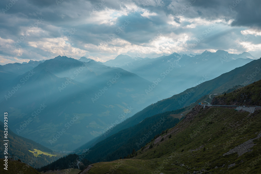 Evening view from the top of jaufenpass looking down towards the sankt leonhard. Sun rays falling through the clouds, epic evening photo in italian dolomites.