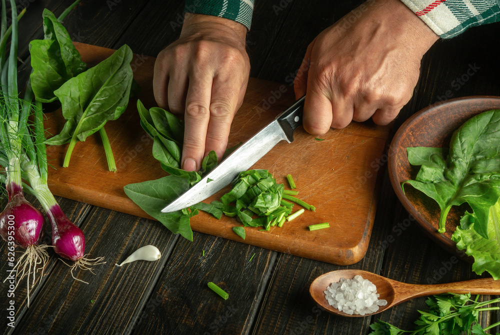 Close-up of a chef hands cut fresh spinach with a knife on a kitchen cutting board. Diet concept of fresh vegetables in the kitchen.