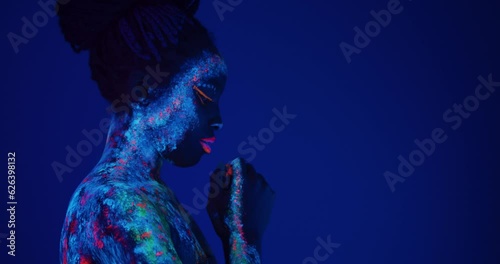 young African American woman looking down and praying Slow motion Body art glowing in ultraviolet light girl asks for blessing. copy space side view