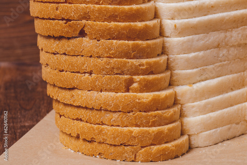 Sliced white bread with brown crust closeup on parchment paper on the wooden table.
