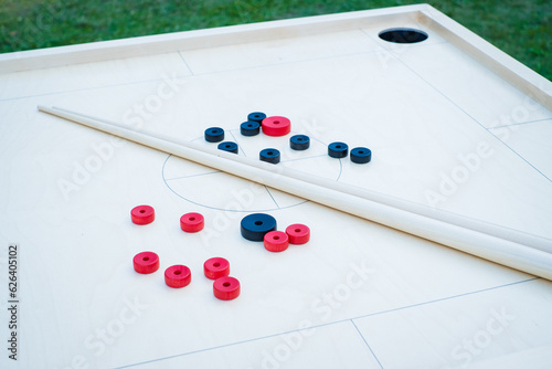 Novuss table with discs and cue stics. Novuss (also known as koroona or korona) is a large wooden board game where small wooden discs are hit with cue sticks into pockets.