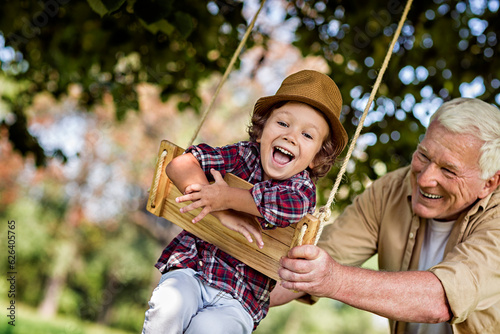 Young boy and his grandfather spending time in the park on a swing