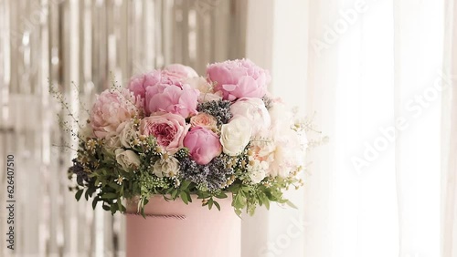 An elegant bouquet of fresh roses, peonies, and daisies in a pink box, beautifully arranged and placed by a light-filled window.