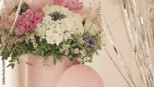 An elegant bouquet of fresh roses, peonies, and daisies in a pink box, beautifully arranged and placed by a light-filled window.