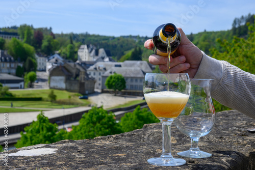 Pouring of blond strong Belgian abbey beer in to glass in sunny day with nice view on old town Bouillon, Belgium photo