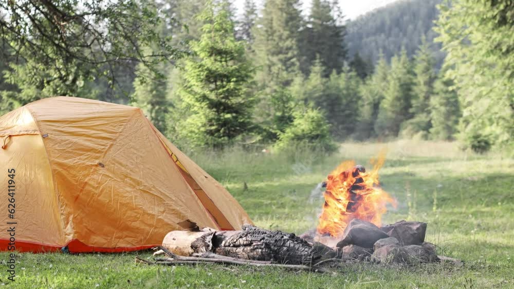A high campfire near tent burns in a campsite by the mountains in beautiful nature. A high campfire near tent burns in a campsite by the mountains in beautiful nature.