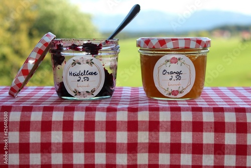 Selbstgemachte Marmelade, gekauft auf dem Wochenmarkt von einer Bäuerin. Heidelbeere und Orange. Allgäu und Bayern Landschaft im Hintergrund.