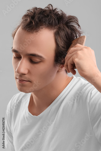 Young man combing hair on grey background, closeup