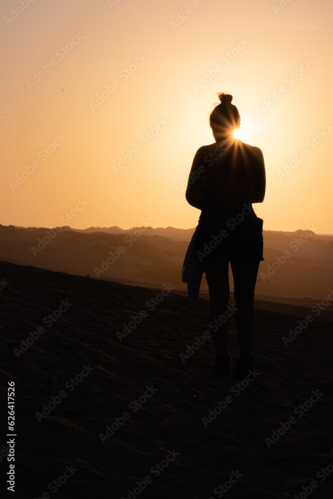 Desert Wanderer: Woman's Silhouette Amidst Dunes at Sunset