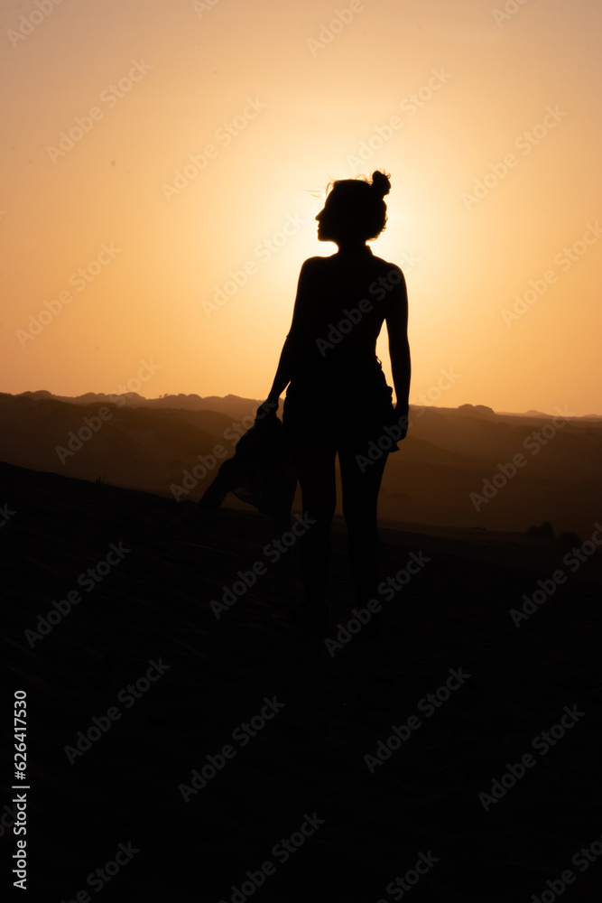 Sunset Stroll: Woman's Silhouette on Desert Dunes with Rising Sun