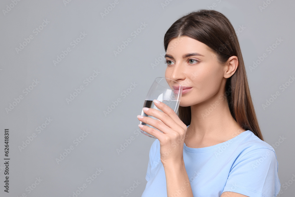 Healthy habit. Woman drinking fresh water from glass on grey background. Space for text Healthy habit. Woman drinking fresh water from glass on grey background. Space for text