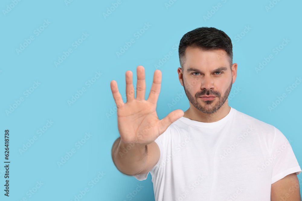 Handsome man showing stop gesture on light blue background, space for text Handsome man showing stop gesture on light blue background, space for text