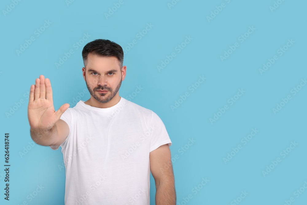 Handsome man showing stop gesture on light blue background, space for text Handsome man showing stop gesture on light blue background, space for text
