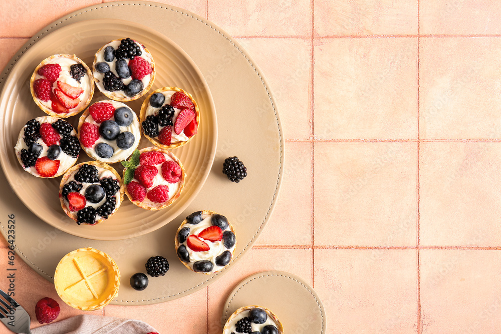 Plate of tasty tartlets with whipped cream and berries on pink tile background Plate of tasty tartlets with whipped cream and berries on pink tile background