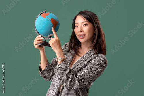 Asian Geography teacher pointing at globe on green background © Pixel-Shot