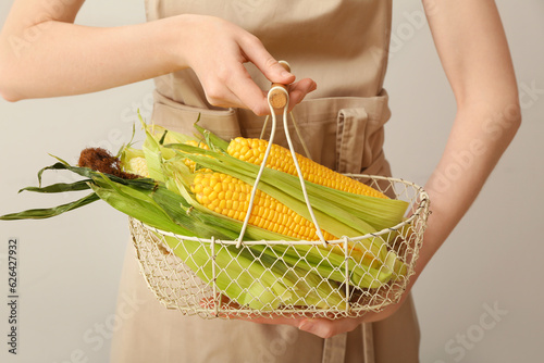 Woman holding basket with fresh corn cobs on white background