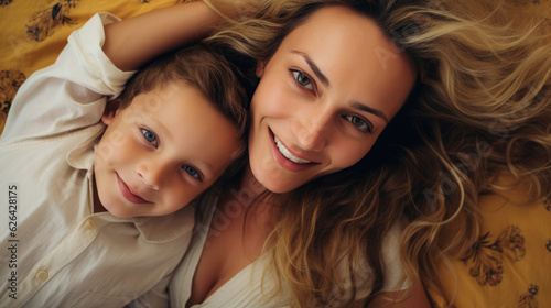 Top view of beautiful woman and her cute little son looking at camera and smiling while lying on the floor
