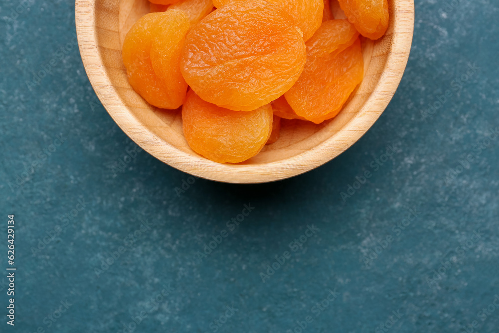 Wooden bowl with tasty dried apricots on blue background Wooden bowl with tasty dried apricots on blue background