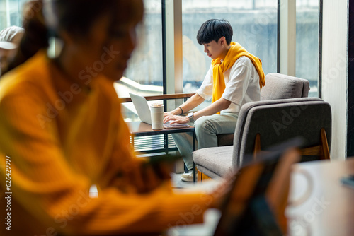 Young Asian man freelancer sitting in cafe in the city working business freelance job on laptop computer and digital tablet. Digital nomad people working from anywhere on gadget device online network.