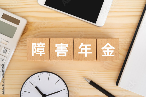 Fotografie 障害年金と書かれたブロック、電卓、スマホ、時計