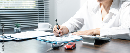 Woman signing car insurance document or lease paper. Writing signature on contract or agreement. Buying or selling new or used vehicle. Car keys on table. Warranty or guarantee. Customer or salesman.