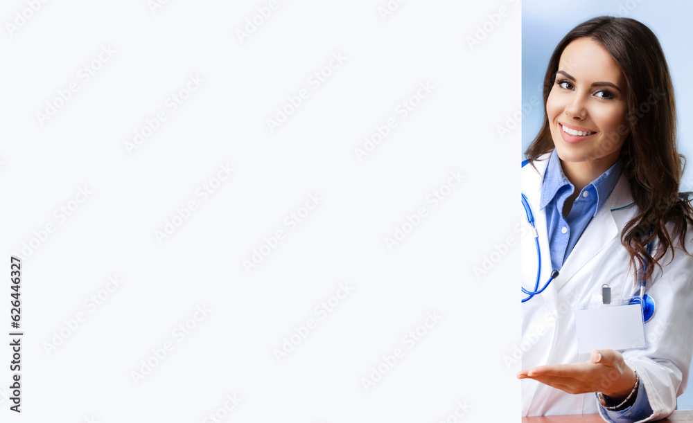 Portrait image of smiling female doctor showing blank signboard with copy space area for some text, at office. Young brunette woman in medical, clinic, healthcare concept