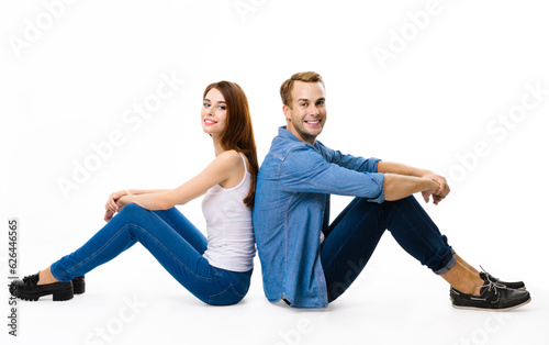 Smiling attractive young couple. Full body profile portrait of sitting back to back models in love studio concept, against white background. Man and woman posing together.