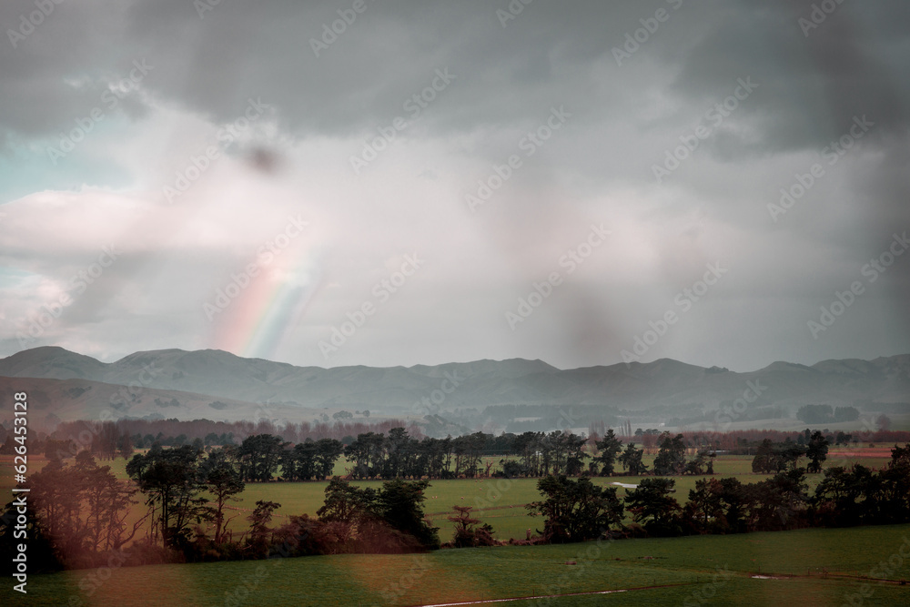 A dark lookinmage of part of a rainbow rising out of a large plain