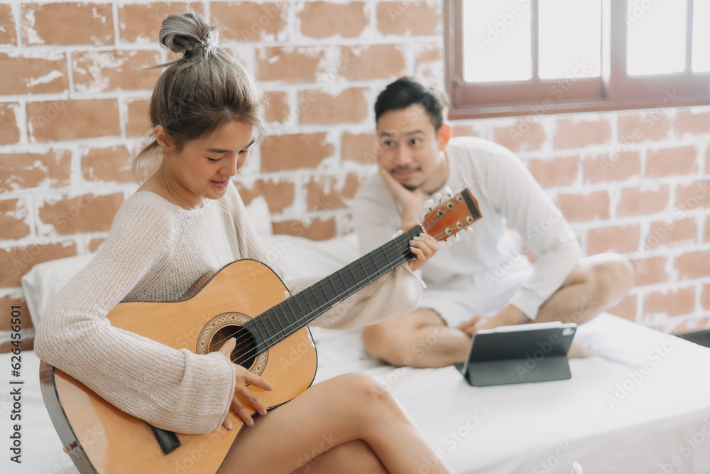 Fototapeta premium Asian man listening to his girlfriend playing guitar on a good hobby weekend.
