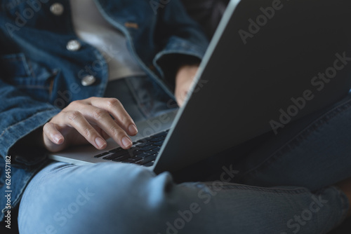 Young casual woman sitting on sofa using laptop computer at home, working from home, close up