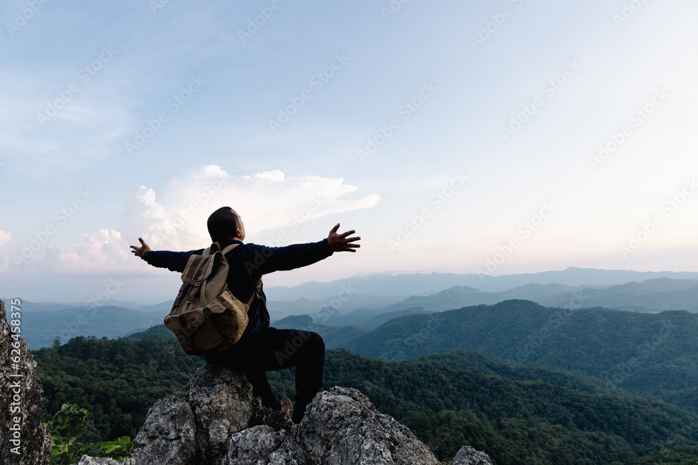 Male tourist on top of rocky mountain. A peaceful man meditating yoga relaxing alone sitting on a mountain top at sunrise with nature landscape. - obrazy, fototapety, plakaty 