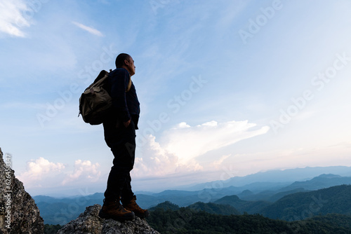 Male tourist on top of rocky mountain. A peaceful man meditating yoga relaxing alone standing on a mountain top at sunrise with nature landscape.