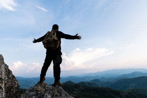Male tourist on top of rocky mountain. A peaceful man meditating yoga relaxing alone standing and spreading arms on a mountain top at sunrise with nature landscape.