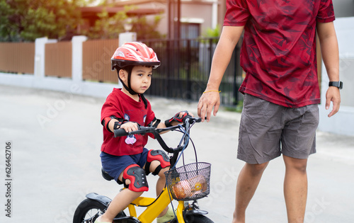 Asian dad teaches son to ride bike, senior helps child, boy in helmet is actively relaxing with his father