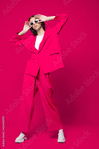 Fashion asian female model in pink suit, white boots and sunglasses.