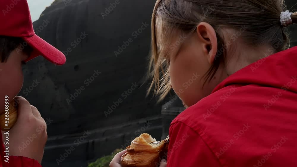 Portrait of two teenagers a boy and a girl eating croissants in the mountains during a snack to recuperate on a hike to the gray rocks of an extinct volcano. View from behind Portrait of two teenagers a boy and a girl eating croissants in the mountains during a snack to recuperate on a hike to the gray rocks of an extinct volcano. View from behind