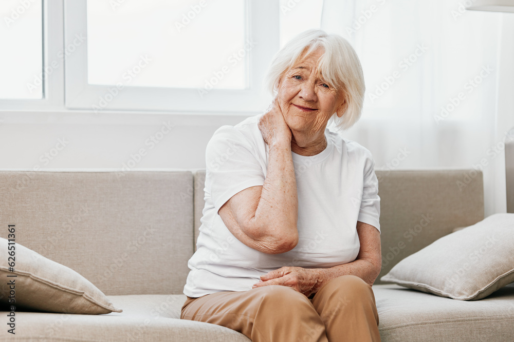 Elderly woman severe neck pain sitting on the sofa, health problems in old age, poor quality of life.