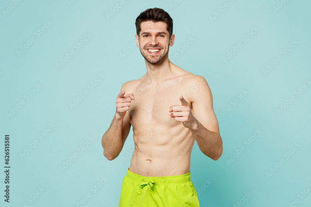 Young man wear green shorts swimsuit relax near hotel pool point index finger camera on you motivating encourage isolated on plain light blue cyan background. Summer vacation sea rest sun tan concept.