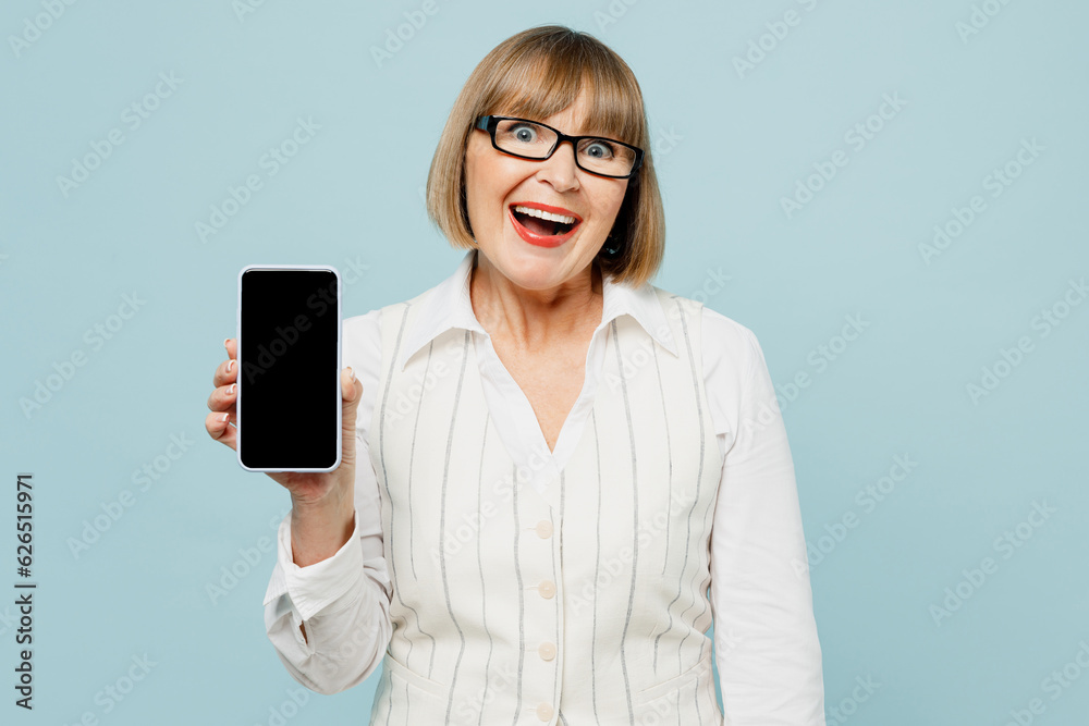 Employee business woman 50s wears white classic suit glasses formal clothes hold use blank screen workspace area mobile cell phone isolated on plain pastel blue background. Achievement career concept.