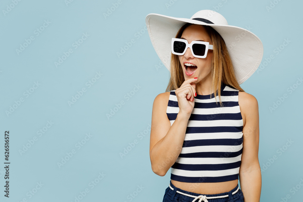 Young surprised happy blonde beautiful woman wear striped tank shirt casual clothes sunglasses hat look aside prop up chin isolated on plain pastel blue background studio portrait. Lifestyle concept. Young surprised happy blonde beautiful woman wear striped tank shirt casual clothes sunglasses hat look aside prop up chin isolated on plain pastel blue background studio portrait. Lifestyle concept.