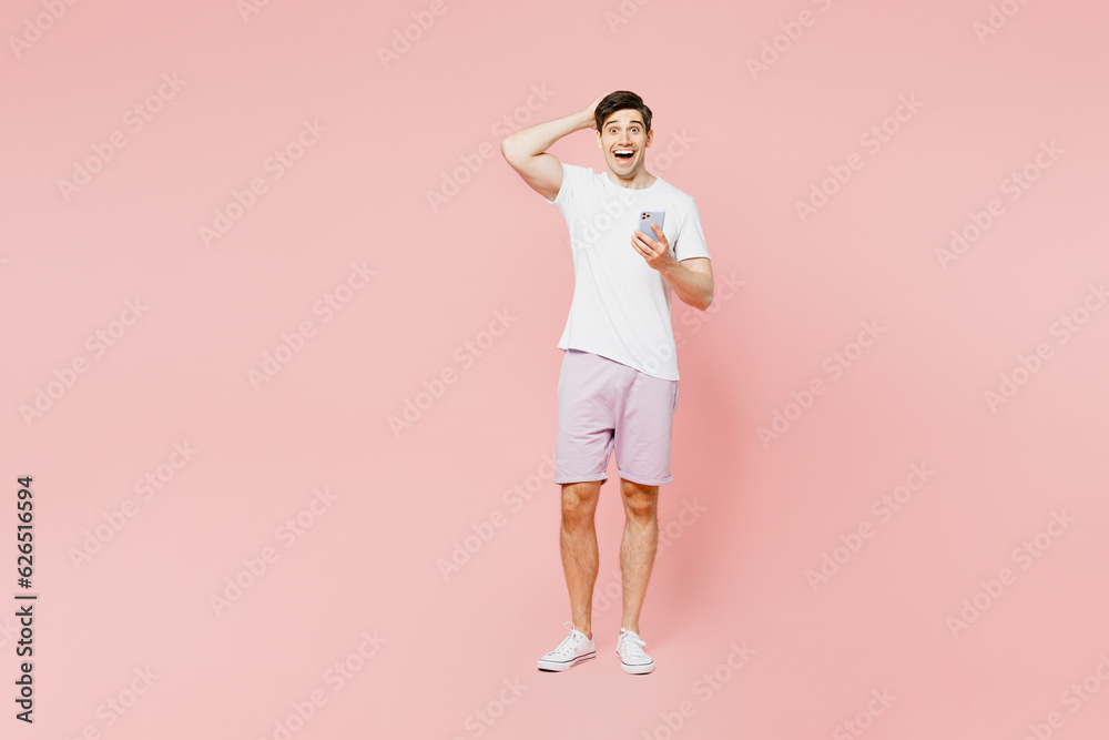 Full body shocked young caucasian man wearing white t-shirt casual clothes use mobile cell phone hold head look camera isolated on plain pastel light pink background studio portrait Lifestyle concept Full body shocked young caucasian man wearing white t-shirt casual clothes use mobile cell phone hold head look camera isolated on plain pastel light pink background studio portrait Lifestyle concept