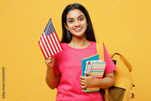 Young smart happy teen Indian girl international student she wear casual clothes backpack bag hold books hold american flag isolated on plain yellow background. High school university college concept. photo