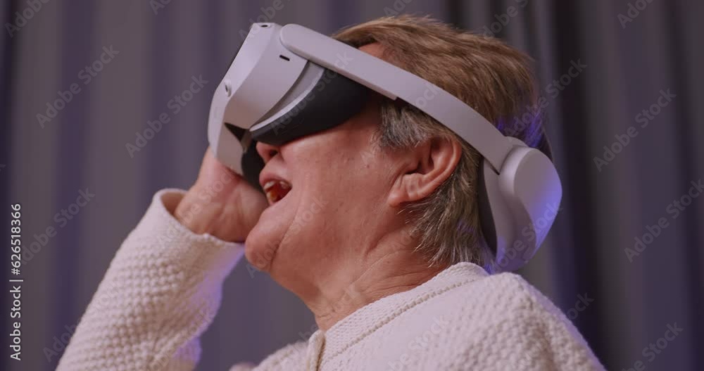 Asian old woman having fun playing games while wearing virtual reality glasses at home.